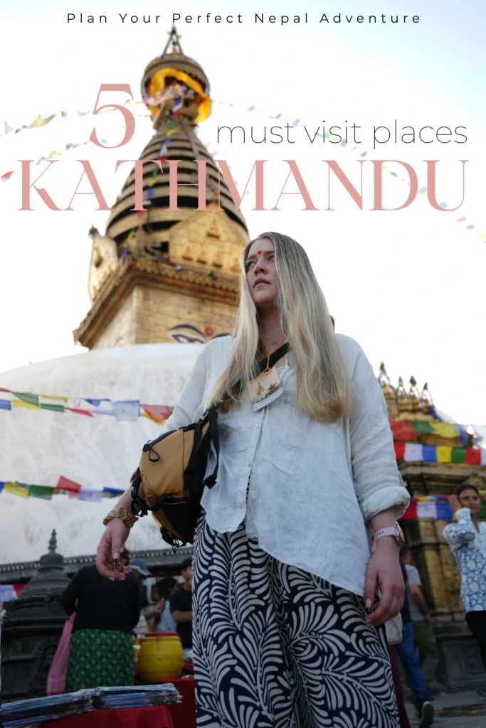 Katmandu: Co Zobaczyć w Stolicy Nepalu? 4 Najlepsze Atrakcje + Gdzie Spać Grafika na Pinterest (Pin) Kobieta z długimi blond włosami i czerwonym tiką na czole stoi przed stupą Swayambhunath (Monkey Temple) w Katmandu, Nepal. W tle widoczne są kolorowe flagi modlitewne, złota wieża świątyni oraz lokalni mieszkańcy i stragany z pamiątkami.
