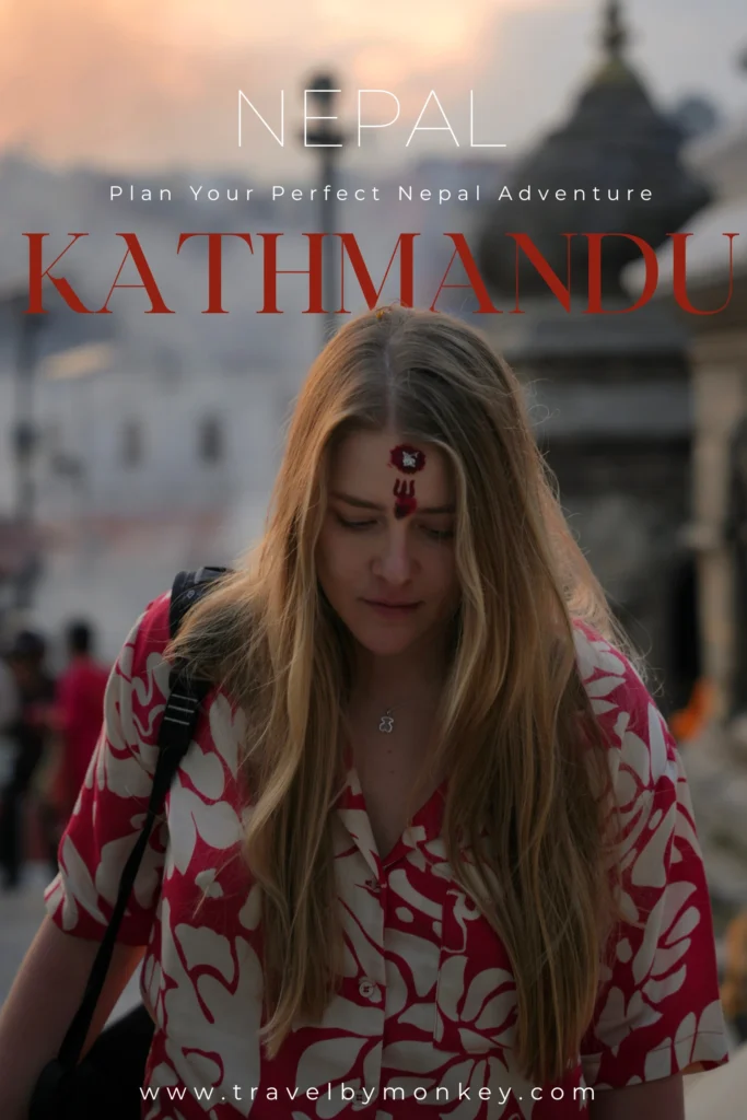 Katmandu: Co Zobaczyć w Stolicy Nepalu? 4 Najlepsze Atrakcje + Gdzie Spać Grafika Pinterest (Pin) Kobieta z długimi blond włosami i czerwonym tiką na czole idzie przez teren świątyni Pashupatinath w Katmandu, ubrana w czerwoną koszulę w białe wzory; w tle widoczne są stupy i światło zachodzącego słońca.