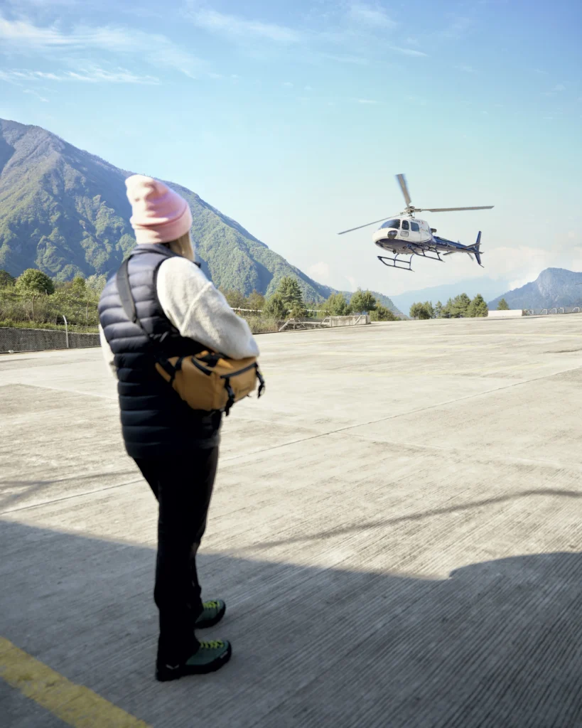 Podróżniczka na lotnisku Lukla w Himalajach obserwująca start helikoptera podczas wycieczki do Mount Everest, Nepal
