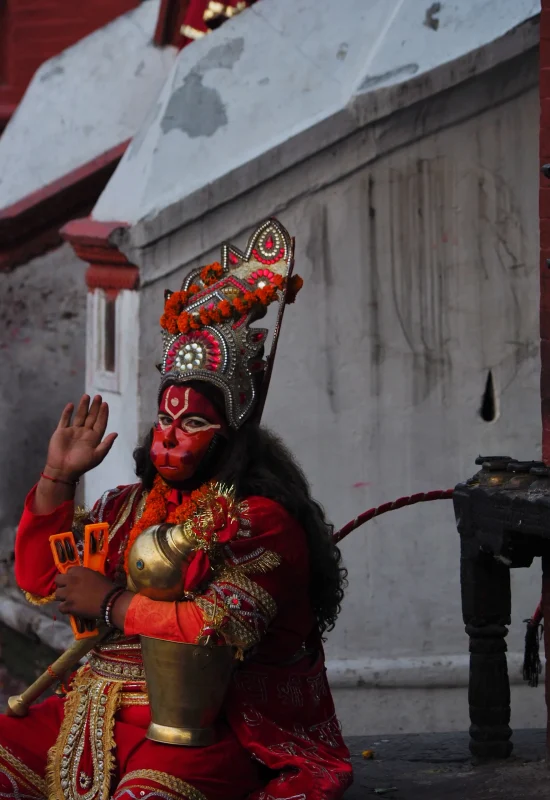 Bog-Malpa-Hinduizm-Pashupatinath-Tempele-Nepal-Katmandu-Zwiedzanie-Kultura-Przewodnik-Co-Robic-Najlepsze-Atrakcje-Street-Photo Przebrany za Hanumana mężczyzna z maską i atrybutami boga małp w świętym miejscu Pashupatinath w Katmandu