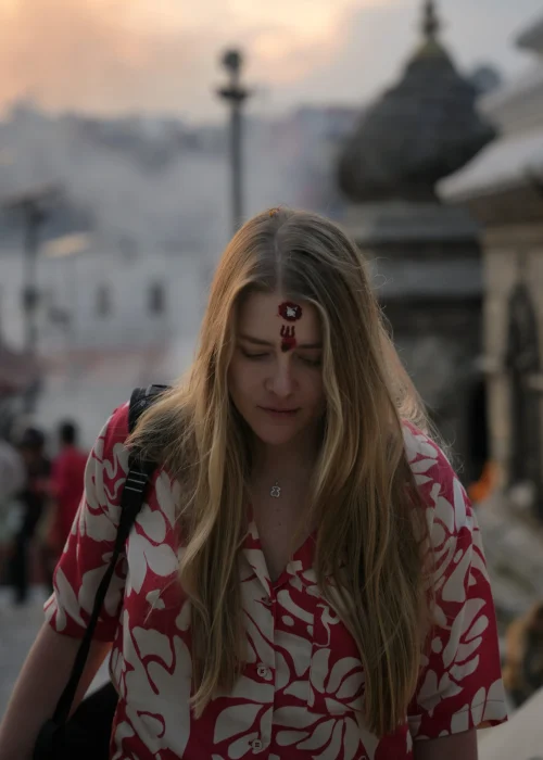 Pashupatinath-Katmandu-Nepal-Zwiedzanie-Przewodnik-Co-Zobaczyc-TKremacje-Rzeka-Bagmati-travelbymonkey Monika z Travel by Monkey w świątynnym kompleksie Pashupatinath z tika na czole i dymem z kremacji w tle, o zachodzie słońca w Kathmandu w Nepalu