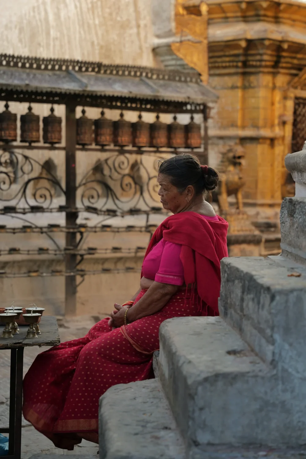 Swoyambhu-Mahachaitya-monkey-temple-ludzie-nepalu-atrakcje-co-robic-architektura-zabutki Nepalka w różowym sari odpoczywająca na schodach świątyni Swayambhunath (Świątynia Małp), obok modlitewnych młynków i ofiarnych lampek